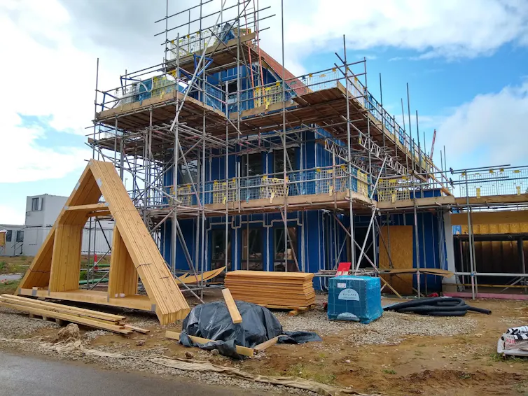 A house being built, surrounding by scaffolding and materials; blue sky.