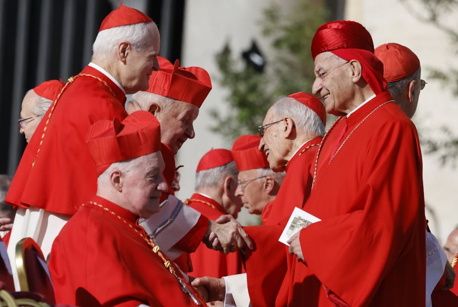 Clergy in red robes and shake hands and greet each other.