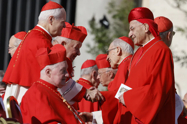 Clergy in red robes and shake hands and greet each other.