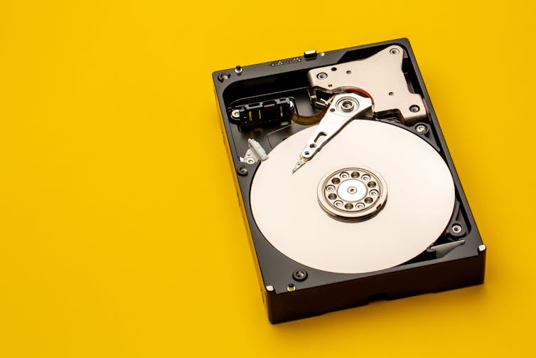 A photo of an opened hard drive on a yellow background.