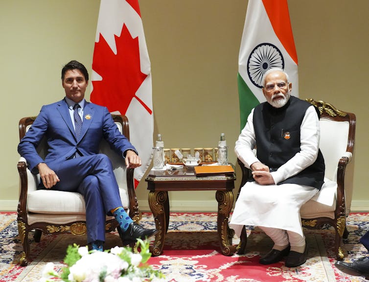 Two men sit in front of the Canadian and Indian flags.