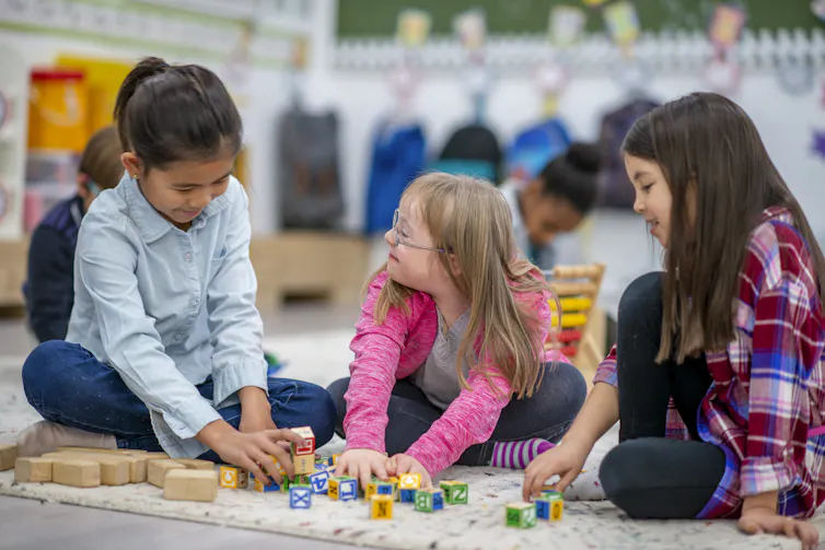 three children play on floor in classroom setting