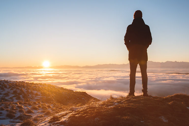 A man stands on the top of a mountain staring at the horizon.