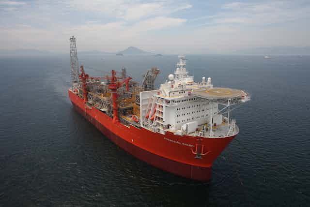 Large red and white ship with helipad, mountains in the background.