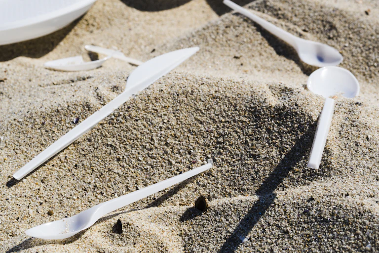 A close-up shot of plastic cutlery on sand at beach.
