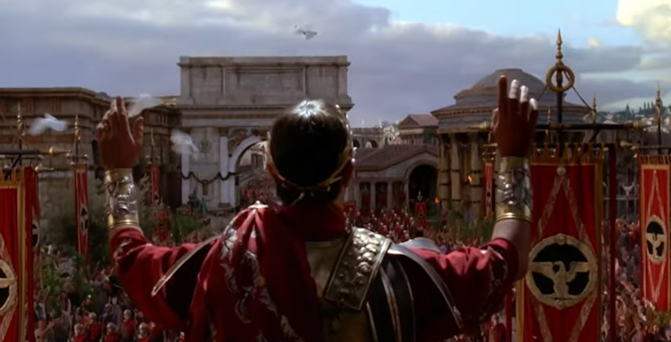 Vemos a un emperador romano de espaldas saludando a su pueblo.