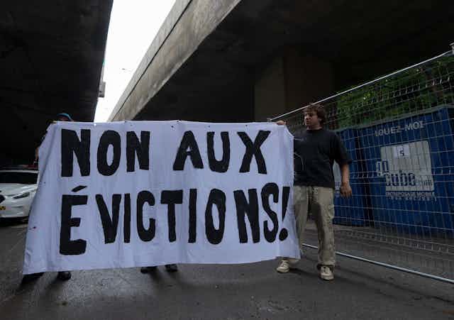 A man holds a sign that reads Non aux évictions!