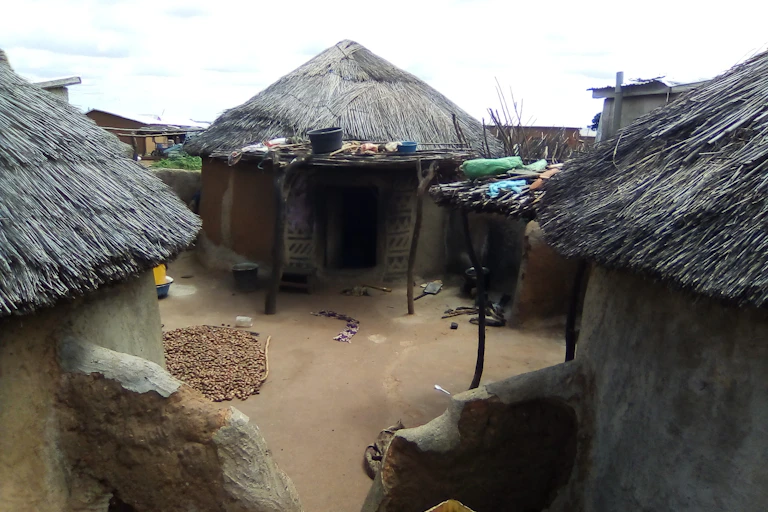 Three thatched huts with bare earth between them.