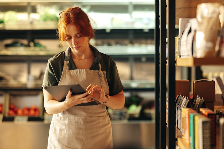 Woman in a apron holding a device, taking stock, supermarket.