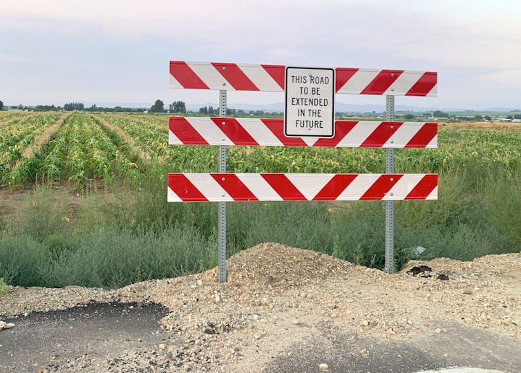A corn field with a road sign reading: 'This road to be extended in the future.' That extension is to build houses in the middle of what is currently a farm field.