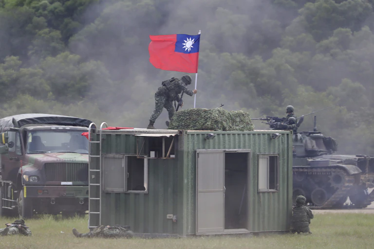 A person in camouflage places a flag atop a metal building.