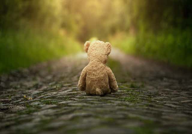 Teddy bear sits alone on cobblestone path