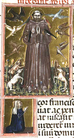 A man in a brown monk's robe stands against a golden backdrop as animals look up toward him.