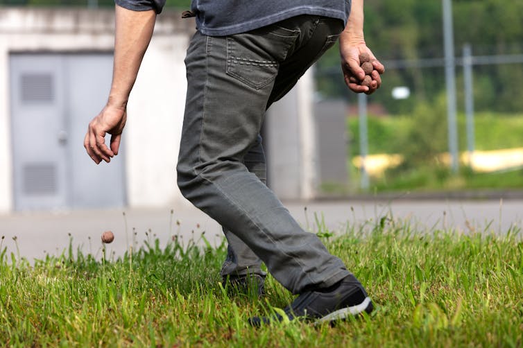 Um homem jogando uma bomba de sementes no chão em frente a um prédio cinza.