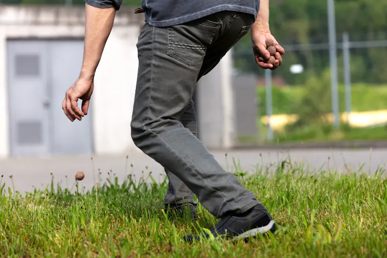 A man dropping a seed bomb on the ground in front of a grey building.