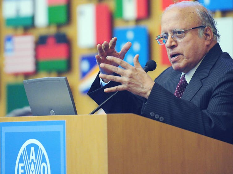 A man in a suit at a podium, speaking and gesturing.