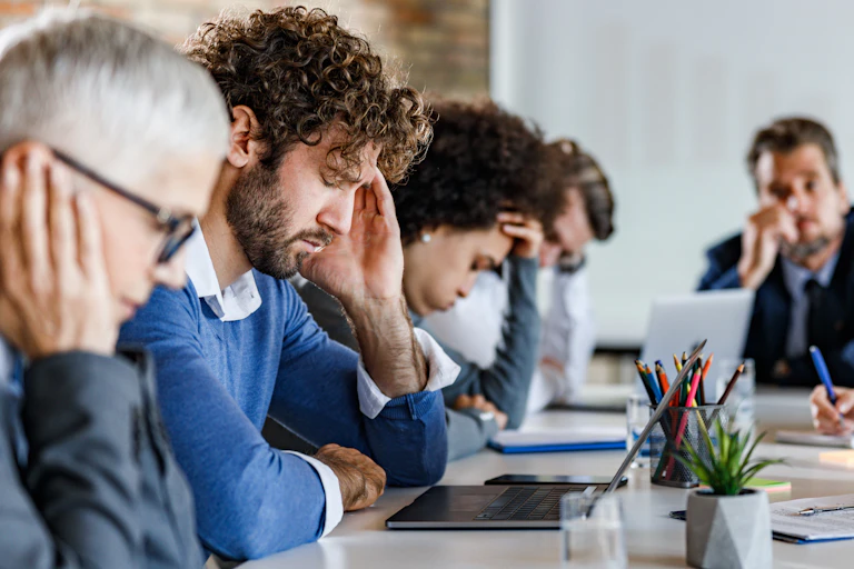 A group of people sit around a table looking exasperated.