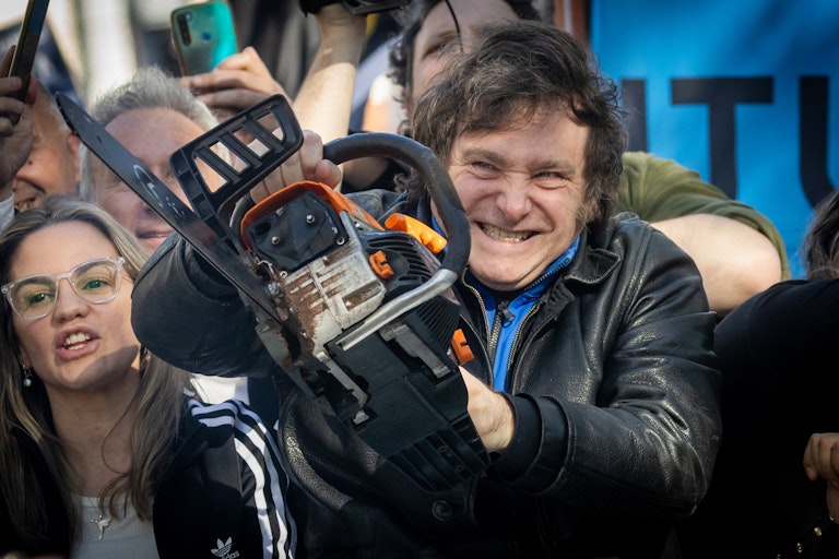 A man with a grin on his face carries a chain saw while surrounded by onlookers.
