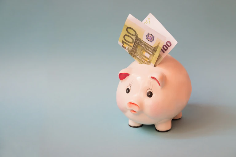 Una hucha de cerdito con un billete de cien euros asomando por ella.