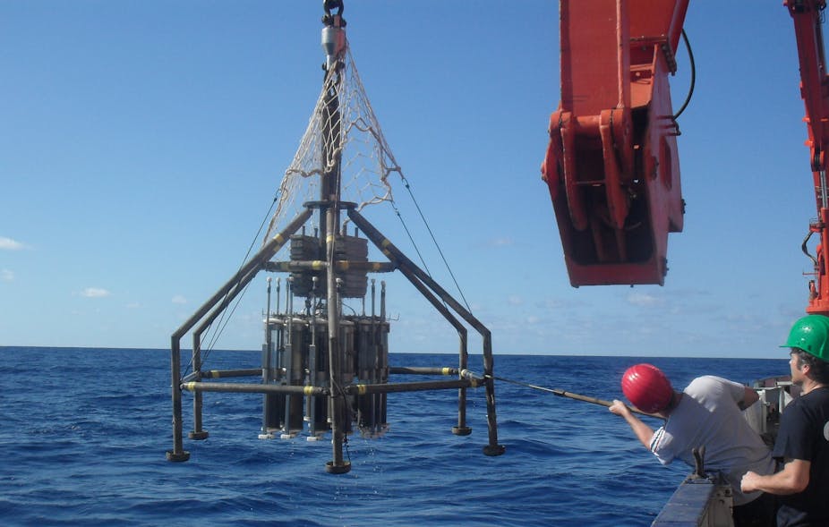 A person in a hard hat uses along pole to steer a robotic contraption over the ocean