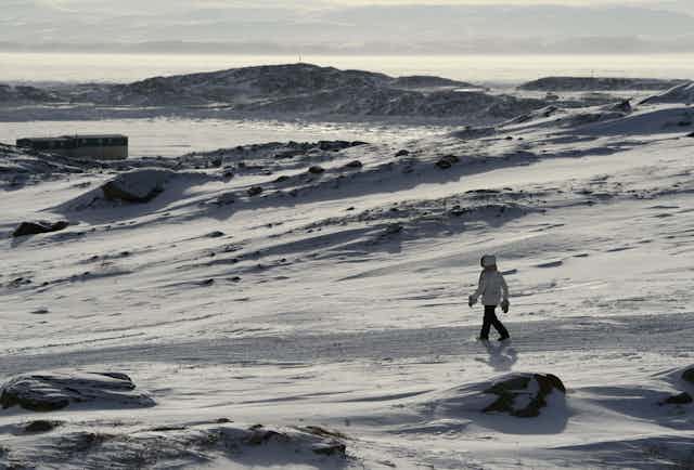 A person in a parka walks across a snowy landscape