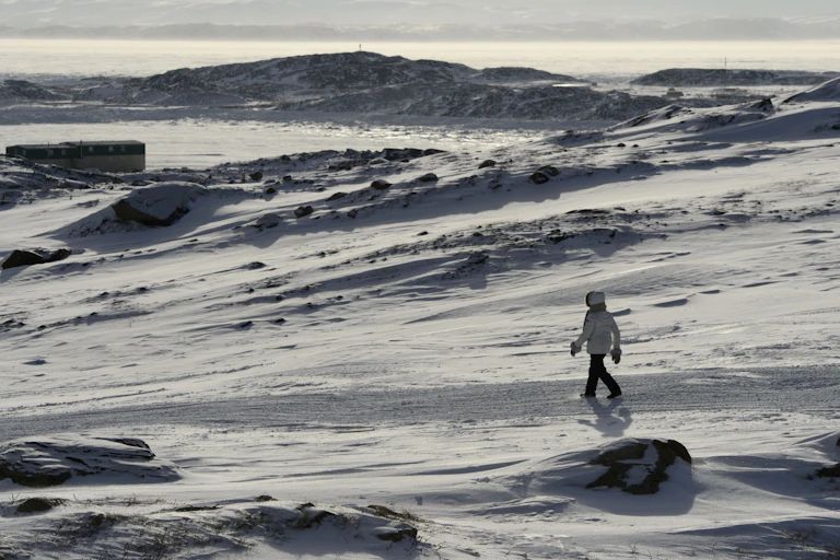 A person in a parka walks across a snowy landscape
