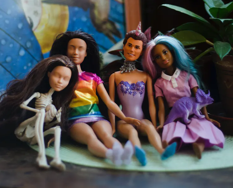A row of Barbie dolls that have swapped parts, one has a skeleton body and a Ken doll has a female body.