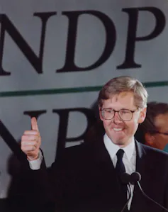 A blond man in glasses smiles while giving the thumb's up.