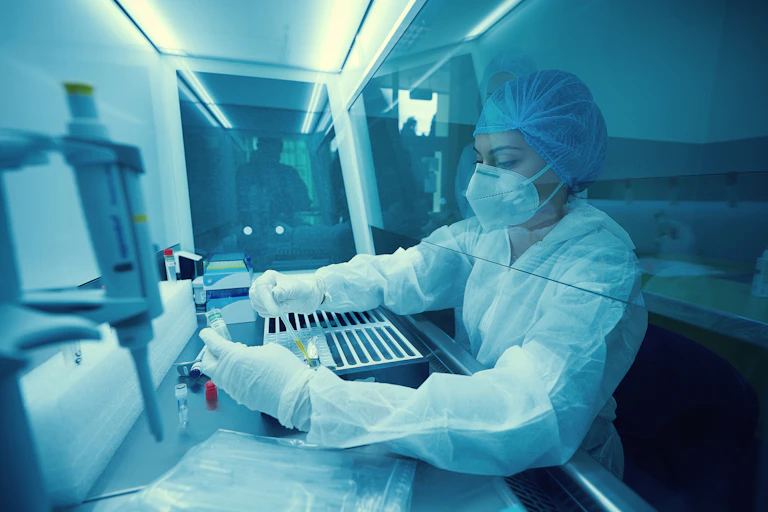 Scientist in full protective equipment pipetting under a fume hood