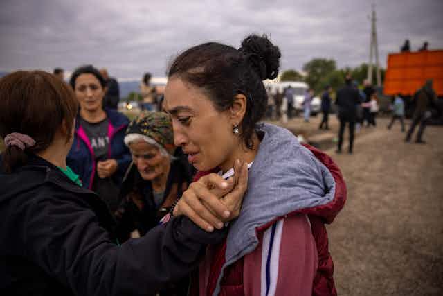 A woman clutches the hand of another in front of a group of refugees.