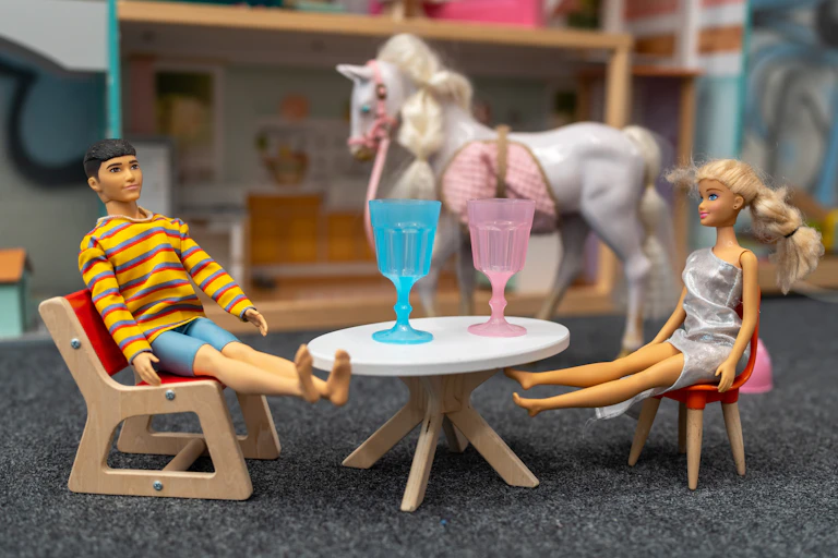 Two dolls seen sitting at a table with giant cups.