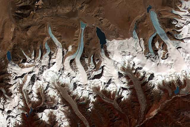 A satellite image shows several glaciers like many fingers down the side of a mountain, and dark glacial lakes at the ends of several of them.