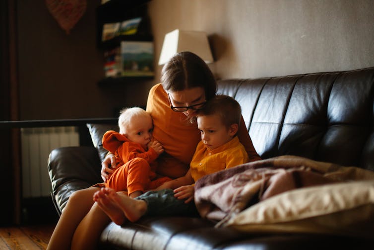 A woman sits on a couch comforting two small children.