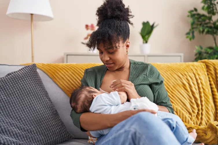 A woman on a couch breastfeeding a baby.