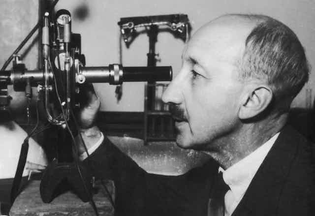 A black and white photo of a man looking through a large microscope