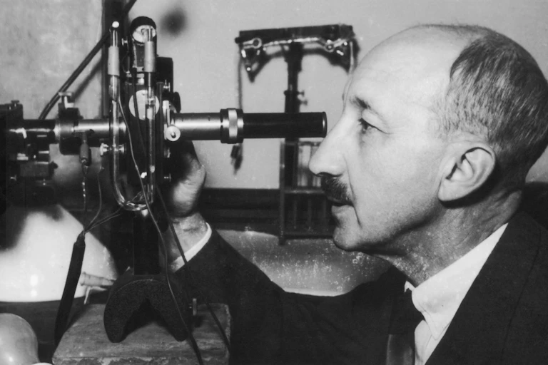A black and white photo of a man looking through a large microscope