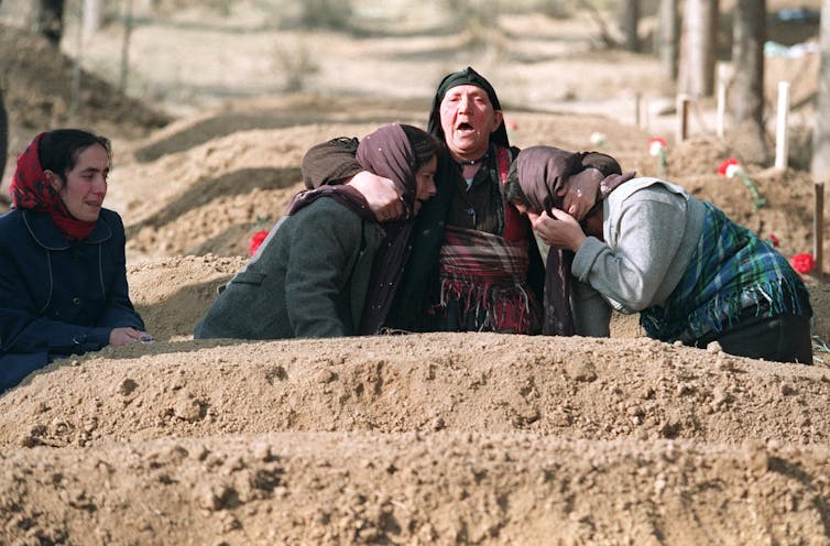 A woman cries out while supported by fellow mourners at a freshly dug grave