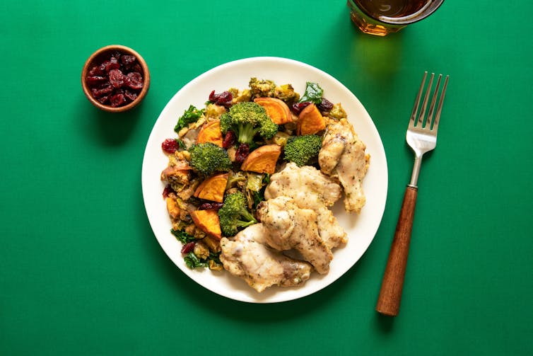 Plate of chicken and veggies, next to a cup of dried fruit