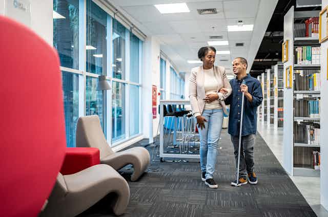 woman walks with visually impaired man through library
