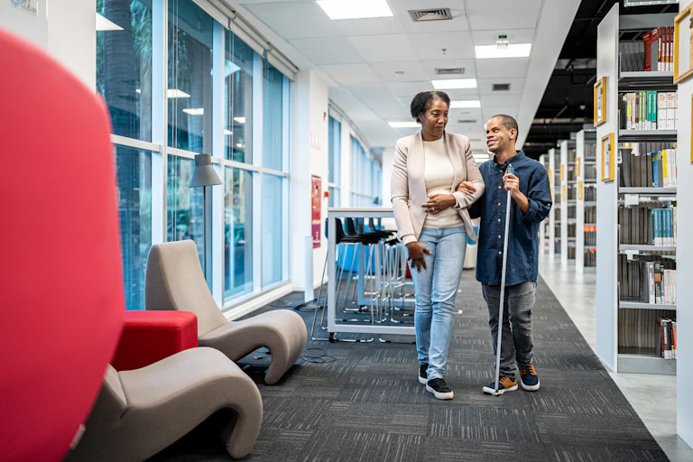 woman walks with visually impaired man through library
