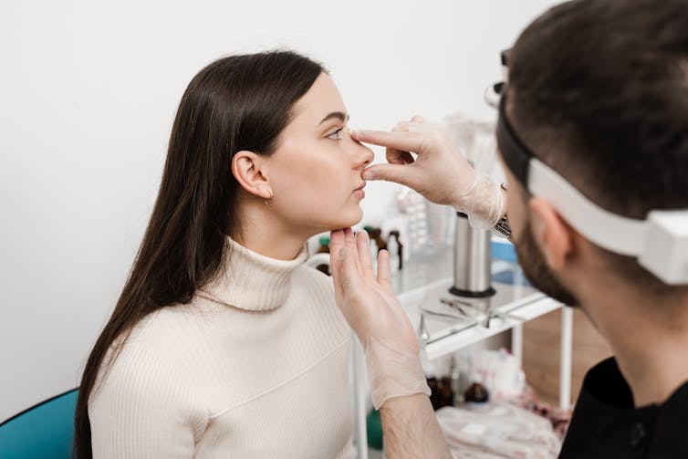 A male plastic surgeon looks at a young woman's nose.