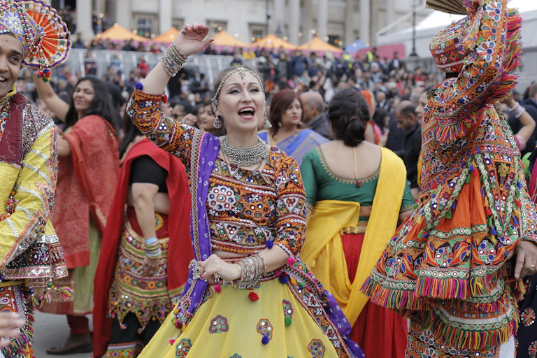 Women and men in brightly coloured traditional clothing dance to celebrate Diwali.