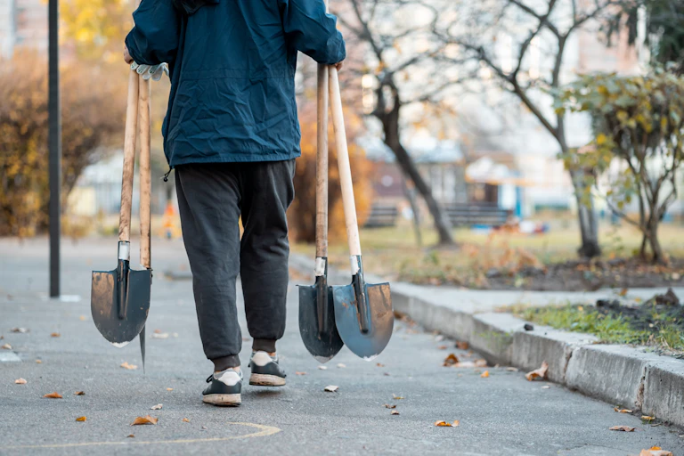 A person carrying shovels down a street.