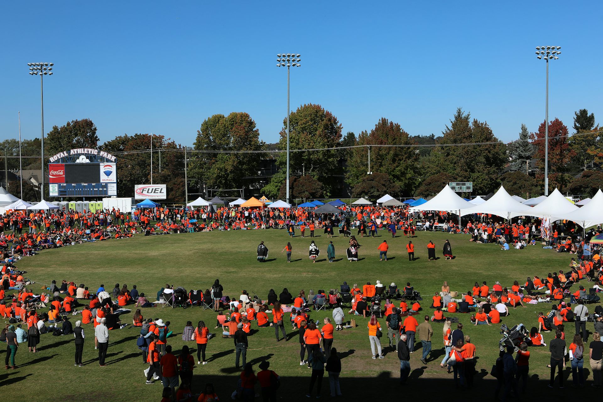 People in orange shirts seen gathering in a circle in a field.