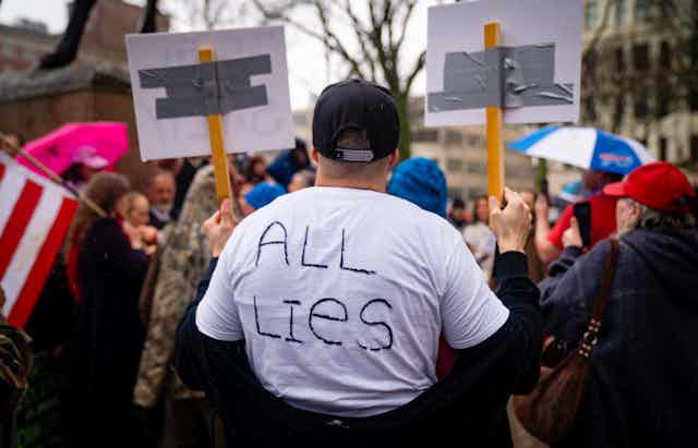 Man at protest with "All lies" written on the back of his white shirt