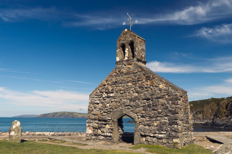 One stone wall of a church stands on a beautiful coastline.