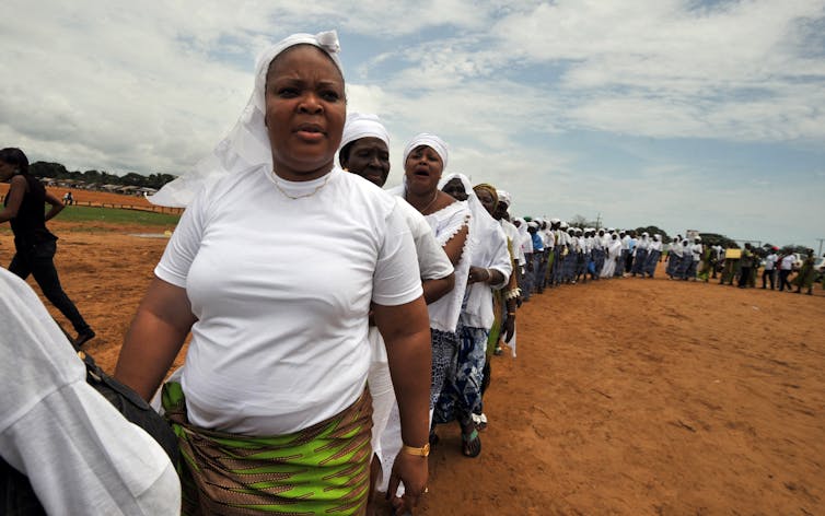 Leymah Gbowee wears a white shirt and marches with a long line of women, also wearing white.