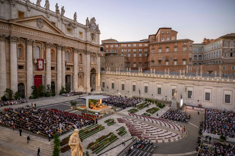 Rows of people sitting in seats formally arranged on the steps outside an ornate stone building.