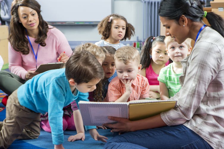 A teacher seen with book and children.