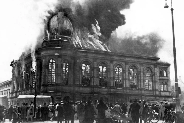 People are gathered outside a large building that is on fire.